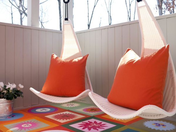 chaise-suspendue-chaises-blanches-et-des-coussins-oranges-au-dessus-d'un-tapis-coloré