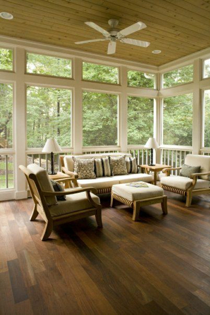 ventilateur-design-plafond-véranda-avec-fenetres-chaises-en-bois-canapés-en-bois-beiges