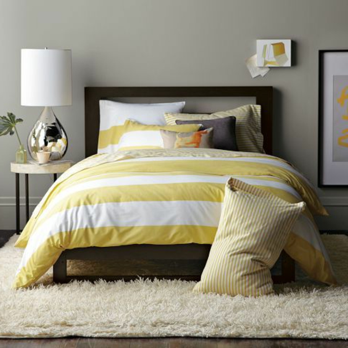 lit-avec-linge-de-lit-coloré-tapis-beige-sol-en-parquette-foncé-mur-gris-peinture