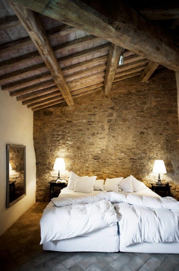 chambre-a-coucher-avec-un-mur-en-pierre-apparente-linge-de-lit-blanc-et-plafond-en-bois-clair