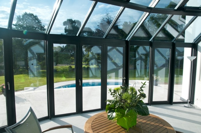 0-bioclimatique-veranda-en-verre-table-en-bois-foncé-belle-vue-vers-le-jaridn-pelouse-verte
