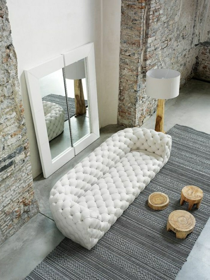 interieur-salon-avec-murs-en-pierres-canape-capitonnée-blanc-en-cuir-blanc-tapis-gris-resized