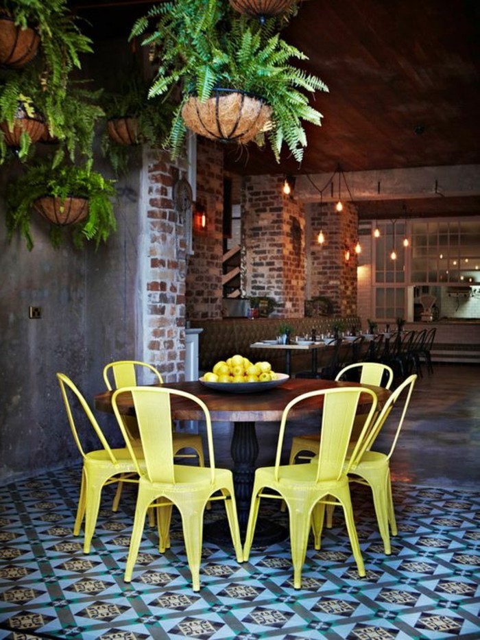 chaises-en-fer-jaunes-sol-en-dalles-colorés-mur-en-briques-table-en-bois-massif-foncé