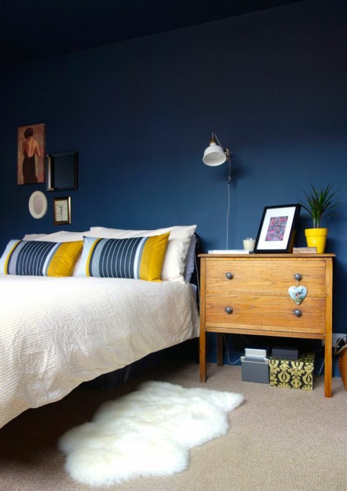 chambre-a-coucher-mur-en-bleu-foncé-table-d-appoint-en-bois-clair-tapis-en-fourrure-blanc