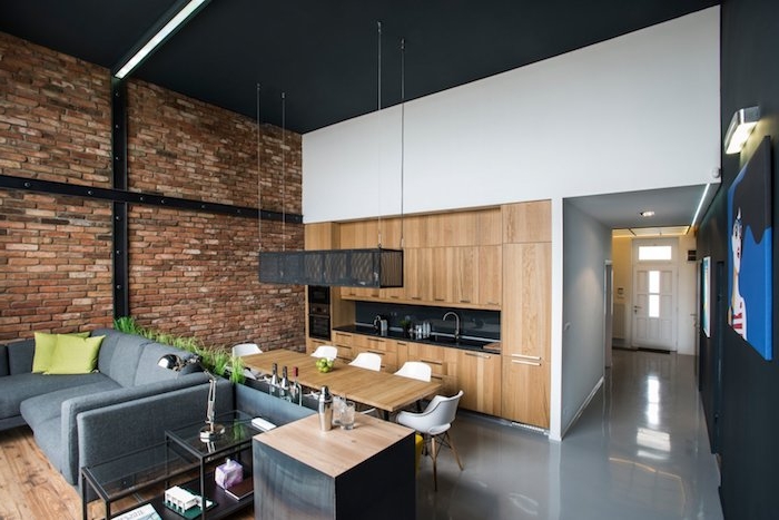 deco loft industriel avec mur de briques, cuisine noire et bois ouverte sur salle à manger avec table bois et chaises scandinaves, coin sejour avec canapé gris