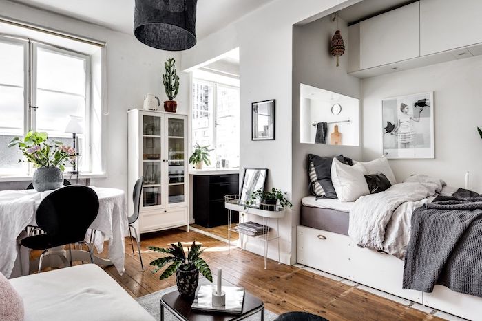 aménager un studio style scandinave avec lit gris et blanc, parquet bois, table à manger entourée de chaises noires, murs blancs