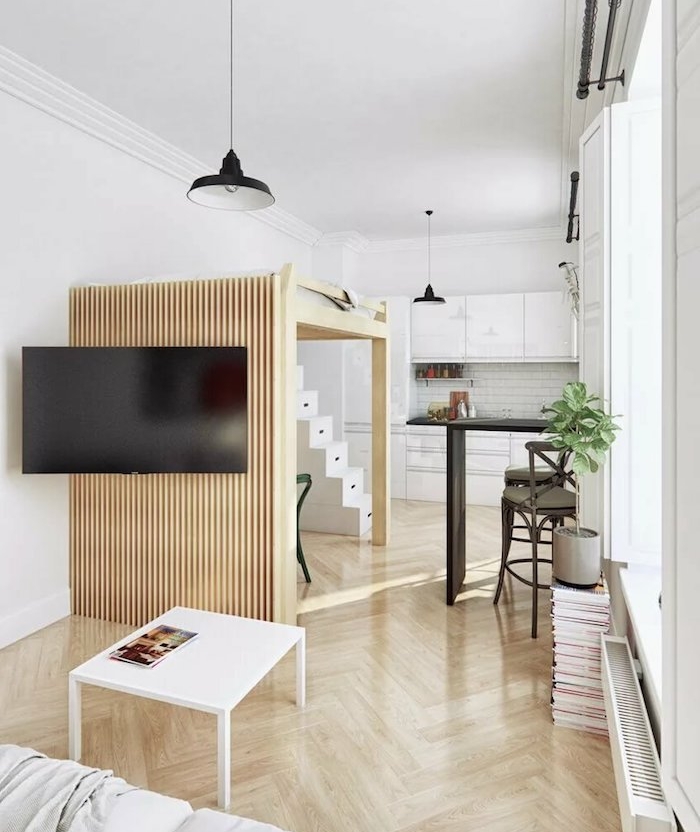 lit surelevé sur une estrade de bois dans un studio blanc et bois avec cuisine kitchenette studio blanche