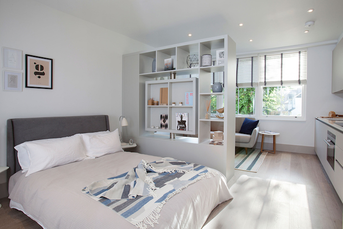 aménagement petit appartement avec lit gris et blanc séparée d un petit coin sejour avec canapé gris, cuisine blanche avec plan de travail noir