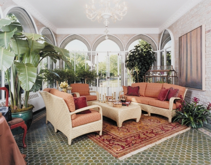 aménagement-veranda-en-coin-de-repos-déco-composée-de-nombreuses-plantes-exotiques-canapé-en-rotin-sièges-oranges-table-à-café-marron-tapis-exotique-lustre-somptueux