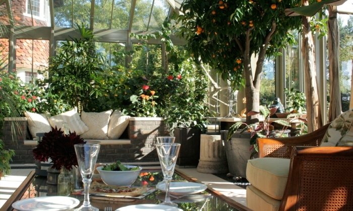 une-magnifique-orangerie-aménagée-avec-beaucoup-de-plantes-table-en-verre-canapé-en-rotin