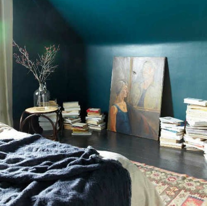 bleu-petrole-dans-la-chambre-a-coucher-murs-bleu-petrole-lit-tapis-oriental-motifs-geometriques-et-floraux-livres-entassés-sur-le-sol-tableaux-d-art-ambiance-chambre-artistique