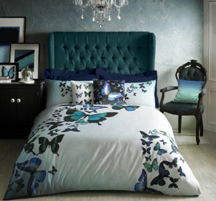 lit-enorme-avec-tete-de-lit-capitonée-bleu-petrole-chaise-tapisserie-bleu-petrole-linge-maison-a-motifs-papillons-papier-peint-bleu-vintage
