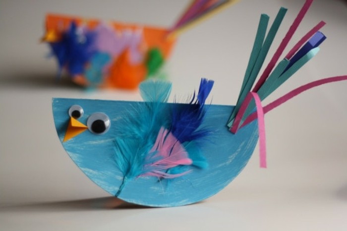 un poussin couleur bleu avec des plumes, des yeux mobiles, bec en papier et queue en bandes de papier, activité manuelle maternelle
