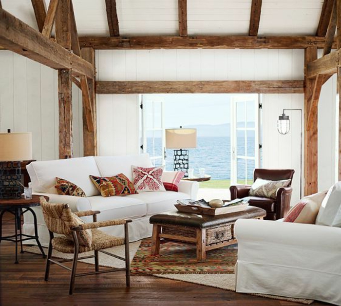 idée déco salon, plafond avec poutres en bois, murs blancs, coussins à motifs ethniques, fauteuil en cuir marron