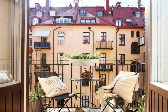 balcon fleuri, chaises noires, table ronde en verre, coussins décoratifs beige