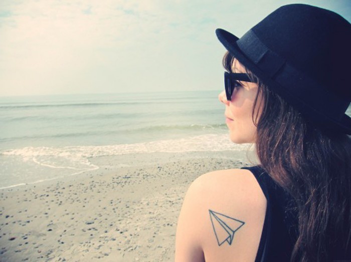 avion en papier tatouage sur l'epaule de fille symbole voyage plage