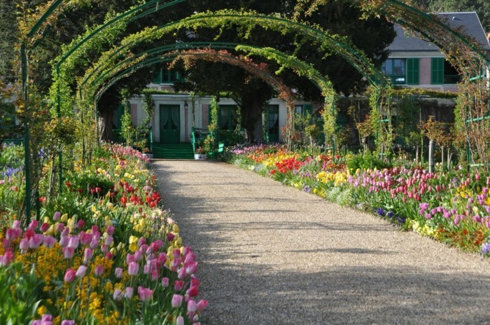 bordure parterre de fleurs, deux rangées de tulipes de couleurs diverses, une tonnelle de jardin, maison rustique de campagne