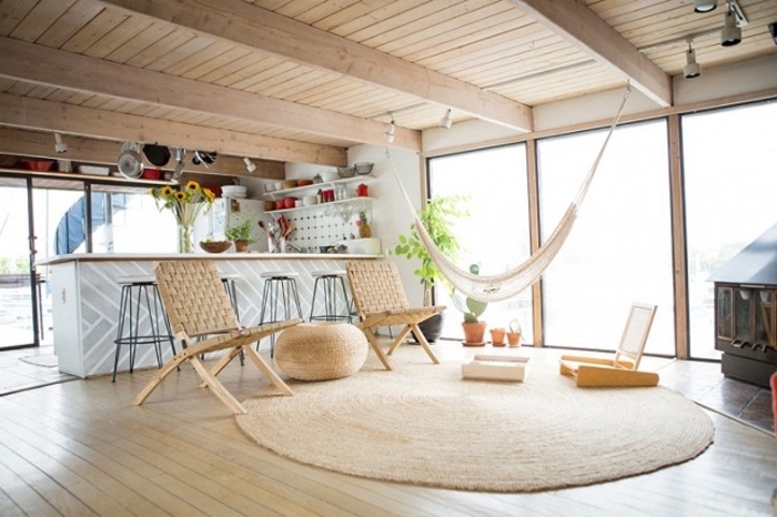 salon cocooning, tapis ronde, hamac blanc, plafond avec poutres en bois, plantes vertes, cheminée