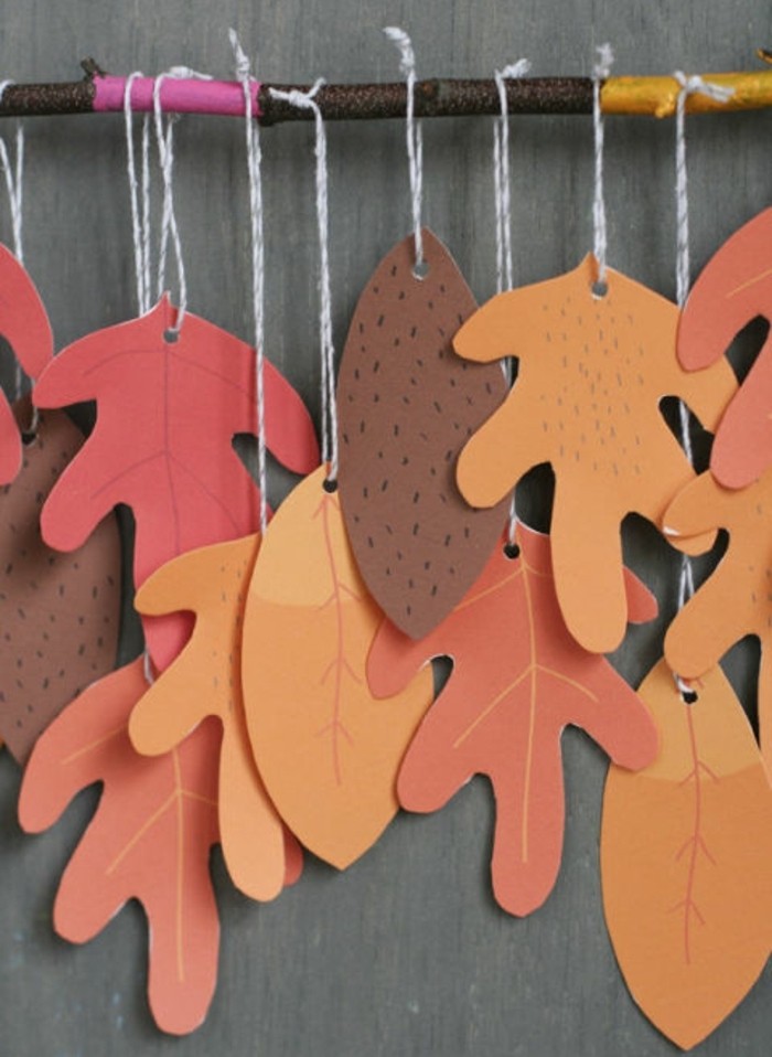 des feuilles mortes en papier orange, rouge, marron, suspendues à une branche, activité manuelle automne maternelle