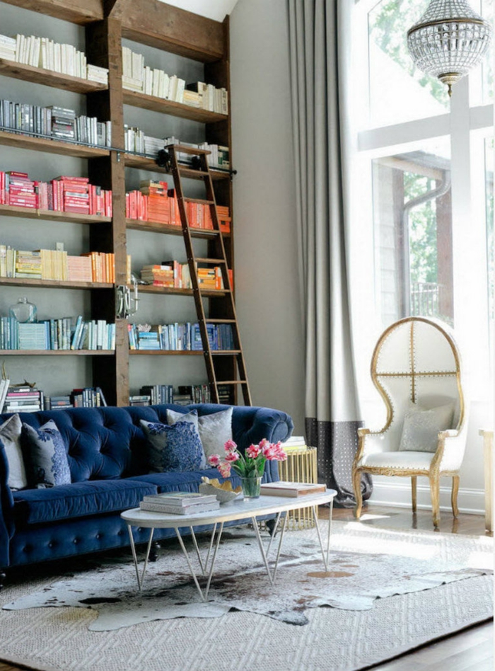 ambiance cocooning, canapé bleu foncé, bibliothèque en bois, rideaux longs, tapis beige