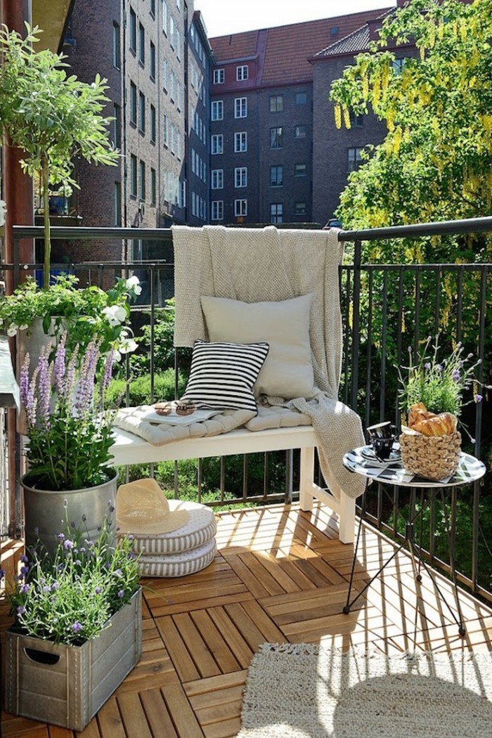 balcon fleuri, sol en bois, petit banc blanc, tapis beige à franges, table ronde en blanc et noir