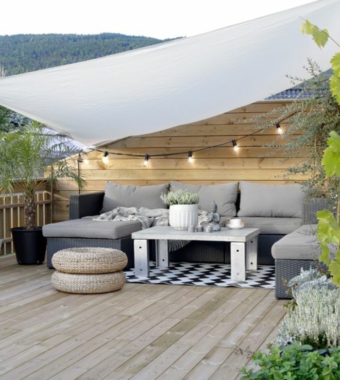 terrasse tropézienne en bois, canapé d angle, pouf, tapis en noir et blanc à motifs géométriques, plantes, guirlande lumineuse, lambris