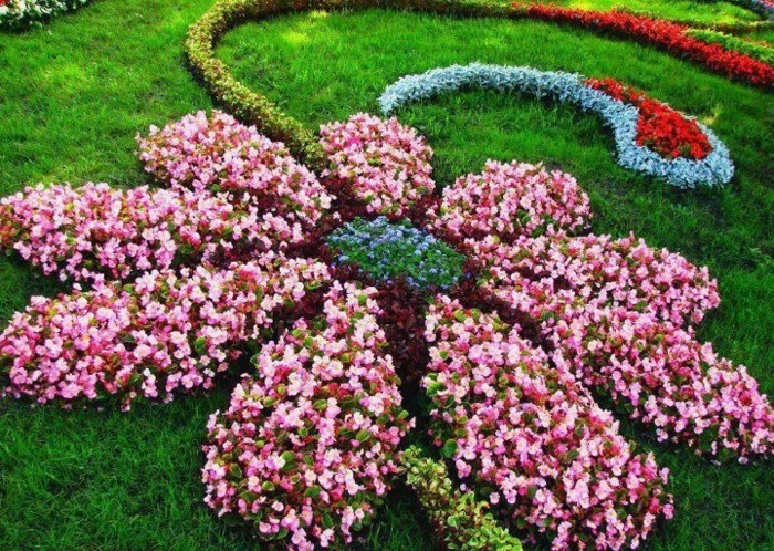 parterre de fleurs en forme de grosse fleur en rouge, rose, bleu et vert, sur une pelouse verte, idée de génie jardin originale