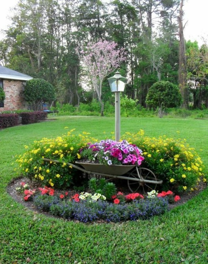 parterre-de-fleur-en-forme-ronde-sur-une-pelouse-fleurs plantées dans une brouette, éclairage extérieur, fleurs de taille et de couleurs diverses