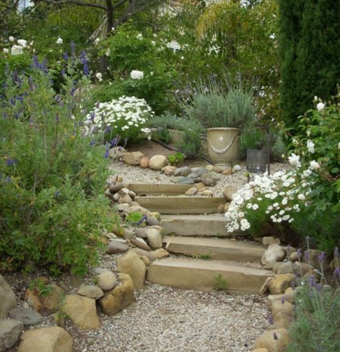 rocaille-fleurie-un-escalier-en-pierre-bordé-de-galets-fleurs-et-arbustes-verts-amenagement-jardin-envahi-par-la-verdure