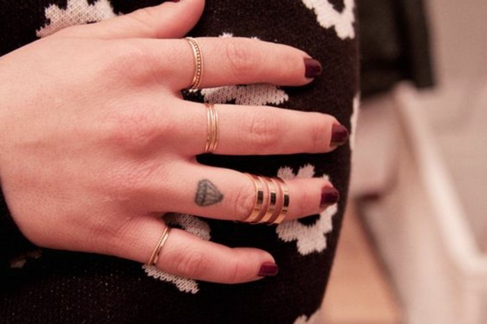 tatouage diamant sur le doigt et une grosse bague demi-doigt