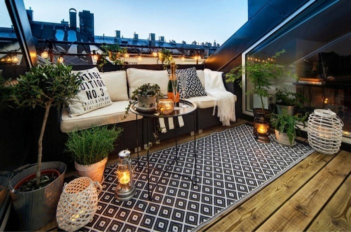 terrasse revêtement bois, taspis en noir et blanc à motifs géométriques, canapé noir avec coussin d'assise et coussins blancs, plantes, terrasse tropézienne