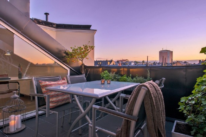 une terrasse tropézienne, carrelage noir, table grise, chaises en métal, plantes, paysage coucher du soleil, coin détente