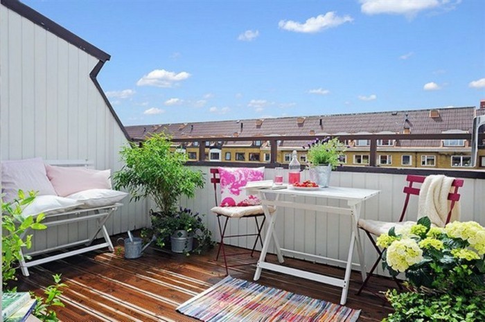 terrasse tropézienne, table blanche en bois et métal, chaises metalliques, plantes vertes, banc en bois pliant, petit tapis multicolore