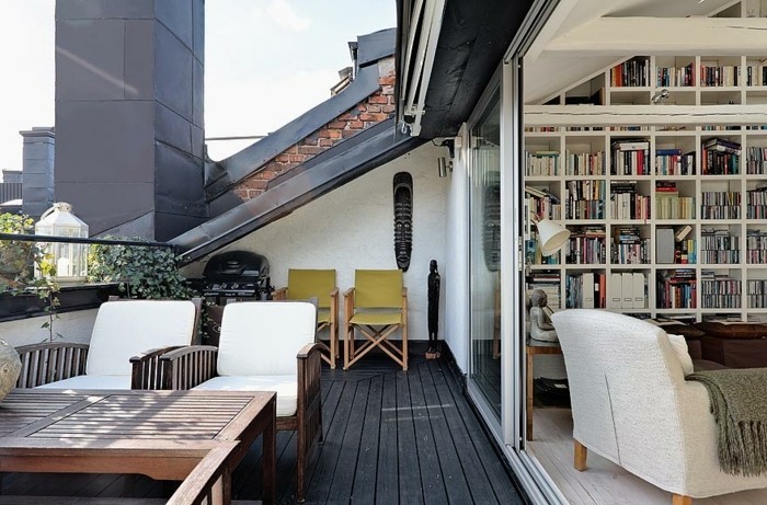 un coin lecture, bibliothèque ouverte sur une terrasse tropezienne, revêtement sol bois composite, table et chaises en bois, deux chaises pliantes