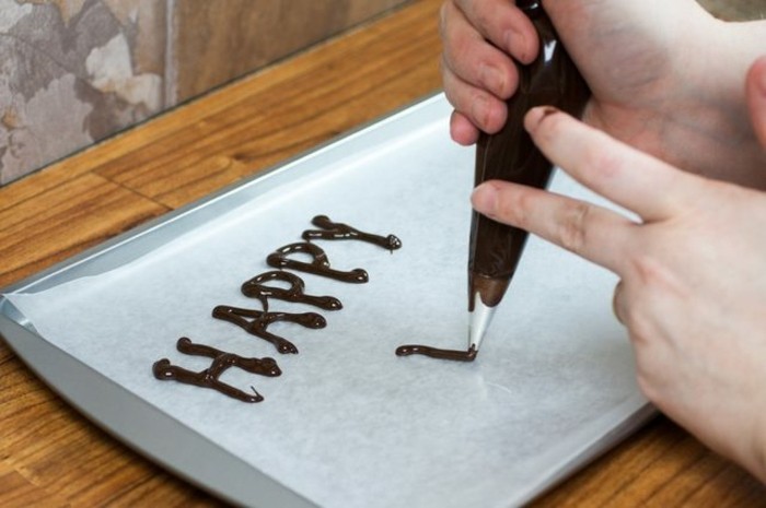 écrire-joyeux-anniversaire-sur-du-papier-sulfurisé-a-l-aide-d-une-poche-a-douille-idee-comment-faire-un-decor-chocolat-sur-un-gateau-d-anniversaire