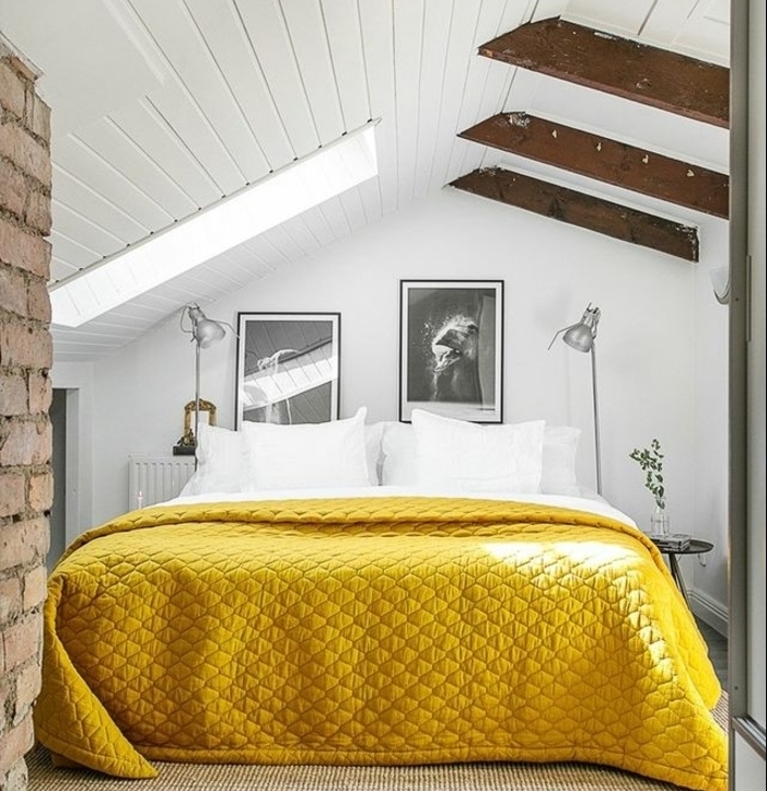 chambre mansardée, couleur mur blanc, deco murale photos en noir et blanc, linge de lit blanc, couverture de lit jaune, poutres apparentes, mur en briques
