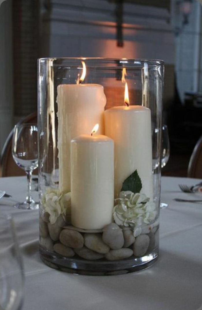 bocaux en verre, galets blancs et bougies blanches allumées mises dans un grand bocal 