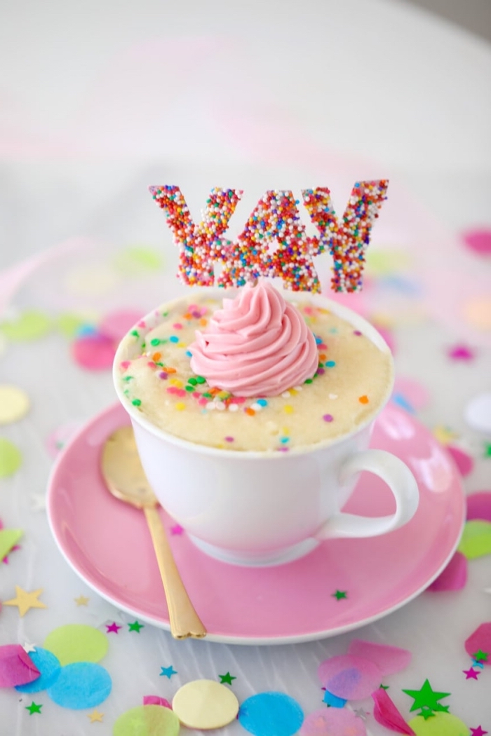 mini cake dans une tasse blanche décoré avec arrose arc en ciel et crème rose, exemple patisserie sans oeuf