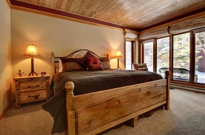 le nid douillet, cadre de lit en bois, grande fenêtre, tapis beige, lampes de chevet, coussins rouges