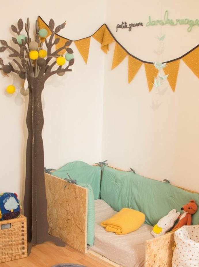 mur couleur beige, lit en bois au sol, matelas, tout de lit, parquet clair, guirlande decorative, decoration arbre en papier, aménagement chambre enfant pédagogie montessori