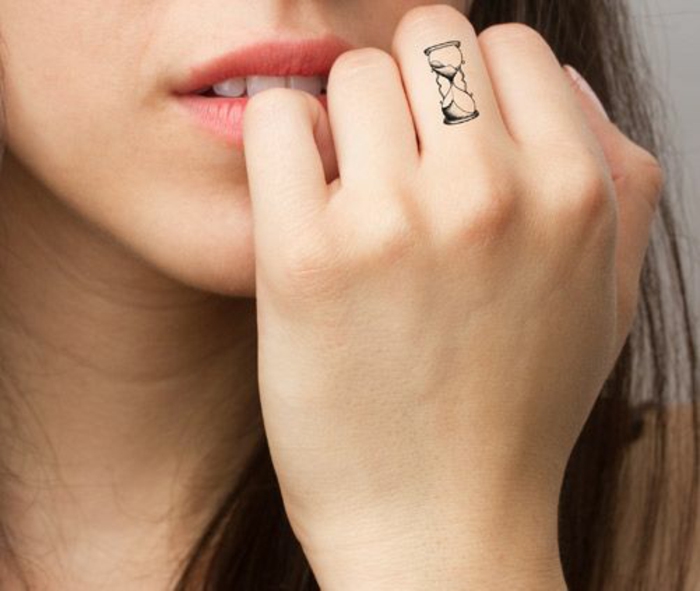 un petit tatouage sur le doigt, un minuscule horloge sablier 
