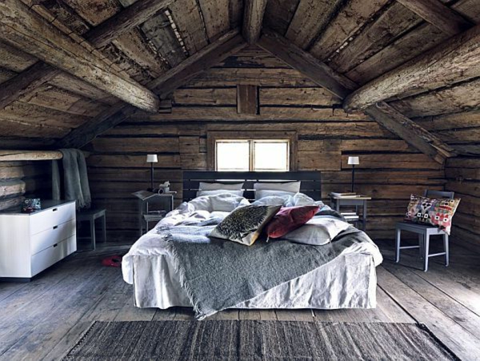 déco chambre sous pente, revêtement sol, toiture en bois brut, linge de lit blanc, couverture de lit grise, coussins multicolores, commode blanc, tapis gris, style rustique
