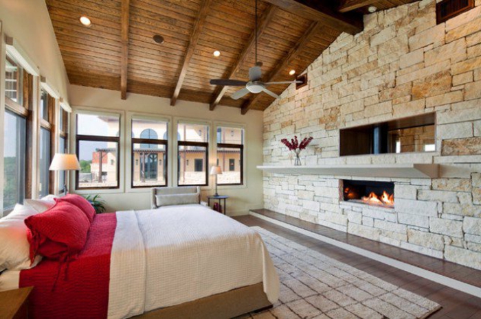 mur d accent en pierres avec cheminée intégrée, amenagemenc combles, chambre à coucher romantique, lit en bois, linge de lit en blanc et rouge, tapis beige, toit mansardé en bois