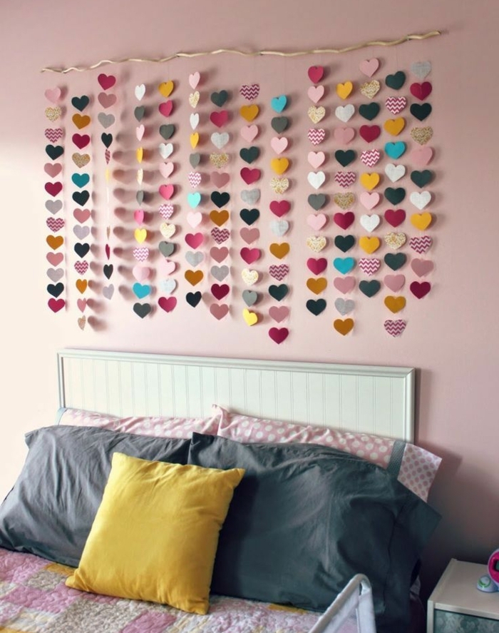 guirlande de papier au dessus d un lit, des coeurs en papier multicolores, suspendus, lit blanc, coussins rose, jaunes et gris, peinture murale rose, idee creation deco, décorer sa chambre