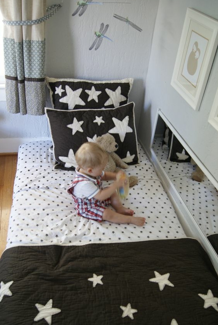 matelas lit bébé à même le sol, blanc à points noirs, couverture de lit, oreillers noirs à étoiles blanches, mur couleur blanche, bébé, jouet ourson