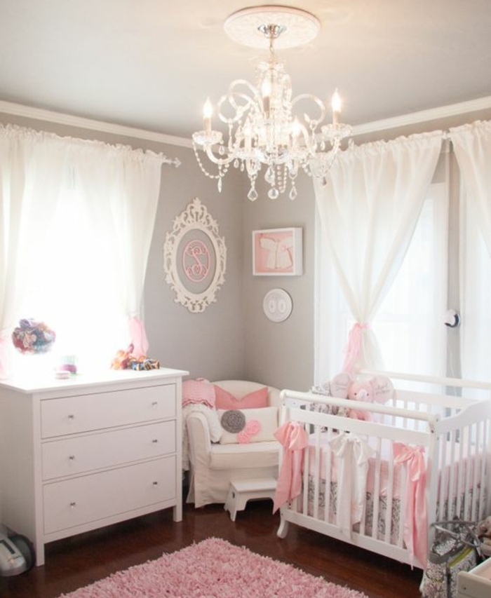 chambre rose et gris, idée aménagement chambre bébé, commode blanc, lit bébé blanc, tapis rose, fauteuil blanc, rubans décoratives rose et coussins rose, parquet marron
