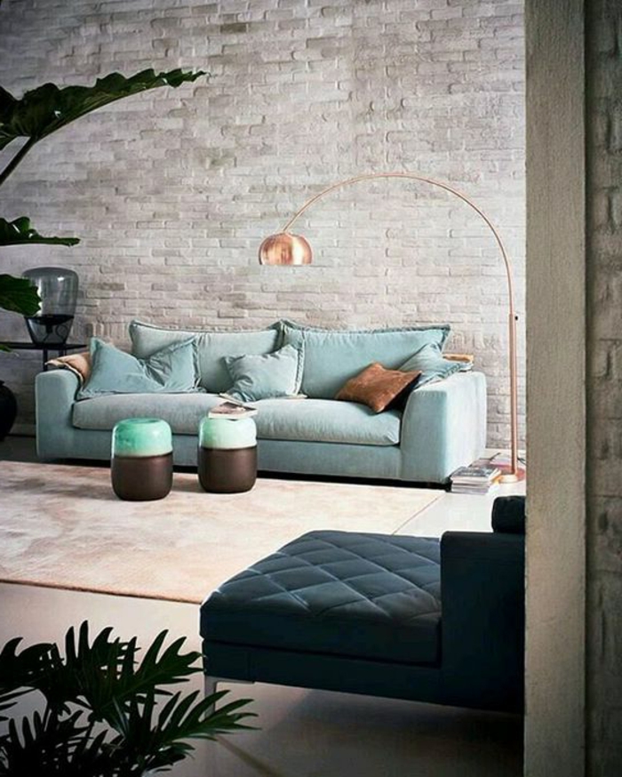 intérieur minimaliste, deux petits tabourets, sofa bleu, lampadaire cuivré, mur en briques