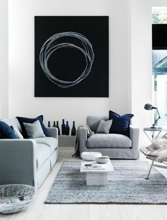 intérieur minimaliste, sofas gris, tableau noir au mur, tapis gris, plusieurs coussins