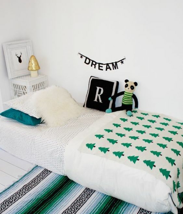 mur couleur blanche, tapis rayures blancs, noirs, couverture de lit motifs sapins, coussin monogrammé, cossins multicolores, jouet panda