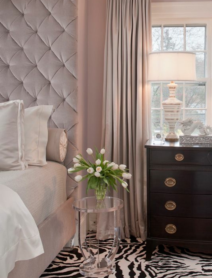 lit rose avec une tete de lit capitonée et linge de lit blanc, commode en bois vintage,tapis zèbre, rideaux rose, peinture chambre adulte rose
